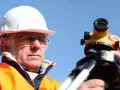 Geodeta w kasku i kamizelce odblaskowej pracuje z niwelatorem. Zastanawiasz się, ile kosztuje geodeta przy budowie domu?
