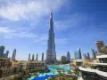 Burj Khalifa, najwyższy budynek świata, na tle błękitnego nieba z chmurami, otoczony nowoczesnymi budynkami i basenem.
