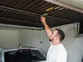 Mężczyzna sprawdza mechanizm bramy garażowej. Czy warto inwestować w garaże i miejsca postojowe przy obecnych cenach najmu?