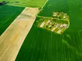Widok z lotu ptaka na pola uprawne i wieś. Różne odcienie zieleni i żółcieni sugerują różne rodzaje gleby, co może pomóc w zrozumieniu, jak sprawdzić klasę gruntu.