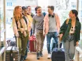 Grupa młodych ludzi z walizkami, śmiejąca się i rozmawiająca. Może to być ich ostatnia wspólna podróż przed zmianami w prawie, **dlaczego od marca 2026 wspólnoty mieszkaniowe mogą nakładać wyższe kary za najem**.