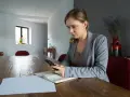 Kobieta z telefonem w ręku przy drewnianym stole. Analizuje dane, szukając odpowiedzi, dlaczego najem średnioterminowy staje się bezpieczniejszą alternatywą dla właścicieli.