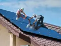 Dwóch monterów instaluje panele słoneczne na dachu. To przyszłość budownictwa, bo od września 2026 r. każdy nowy budynek musi posiadać magazyn energii.