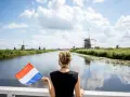 Kobieta z holenderską flagą podziwia wiatraki, marząc o tym, jak znaleźć mieszkanie w Holandii.