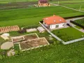 Budowa domu w toku: fundamenty, sterty cegieł i materiałów budowlanych. Obok gotowy dom i pole. Ile arów musi mieć działka budowlana?