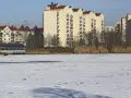 Zimowy krajobraz z zamarzniętym jeziorem i blokami mieszkalnymi w tle. Czy to zapowiedź, dlaczego ceny mieszkań w Warszawie mogą spaść nominalnie do końca 2026 roku?
