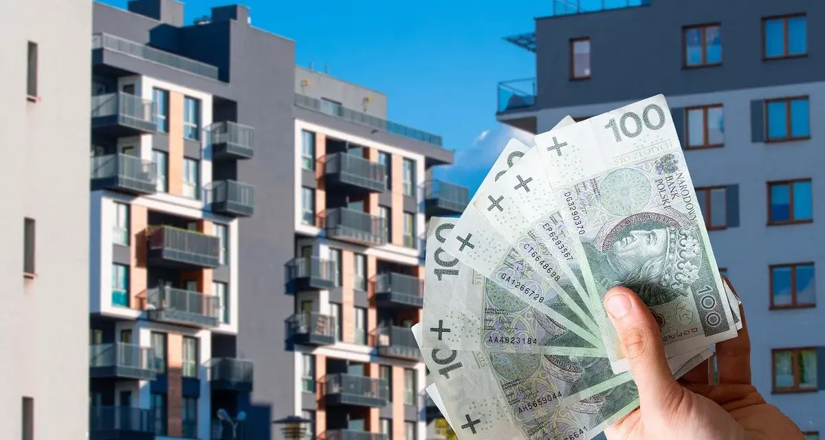 Dłoń trzyma banknoty 100 zł na tle nowoczesnych bloków mieszkalnych. Czy to wyjaśnia, dlaczego ceny najmu w Warszawie i Krakowie przestały rosnąć w pierwszym kwartale 2026?