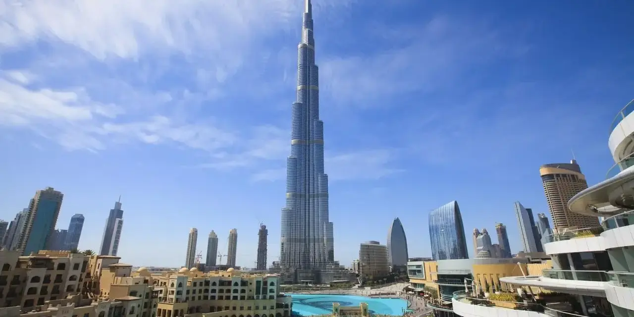 Burj Khalifa, najwyższy budynek świata, na tle błękitnego nieba z chmurami, otoczony nowoczesnymi budynkami i basenem.