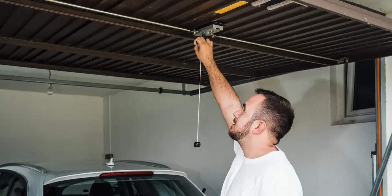 Mężczyzna sprawdza mechanizm bramy garażowej. Czy warto inwestować w garaże i miejsca postojowe przy obecnych cenach najmu?