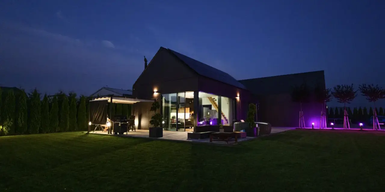 Nowoczesny dom nocą, z oświetlonym ogrodem i tarasem. Analiza prawdziwych kosztów eksploatacji domów pasywnych w polskich warunkach klimatycznych.