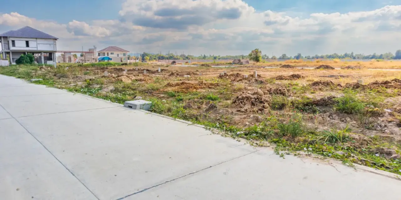 Budowa domu wkrótce? Zastanawiasz się, ile kosztuje metr działki budowlanej? Teren pod zabudowę z fundamentami i domami w tle.