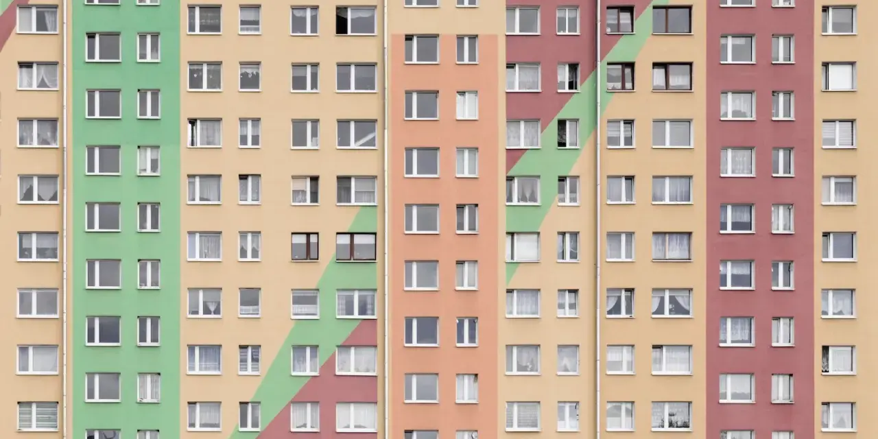 Wielopiętrowy blok mieszkalny w kolorach pastelowych. Szukasz informacji, jak wynająć mieszkanie komunalne?