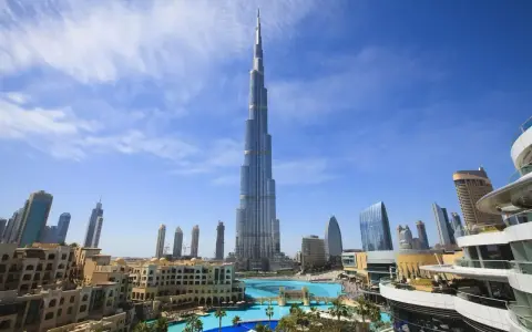 Burj Khalifa, najwyższy budynek świata, na tle błękitnego nieba z chmurami, otoczony nowoczesnymi budynkami i basenem.