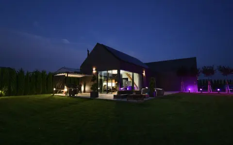 Nowoczesny dom nocą, z oświetlonym ogrodem i tarasem. Analiza prawdziwych kosztów eksploatacji domów pasywnych w polskich warunkach klimatycznych.