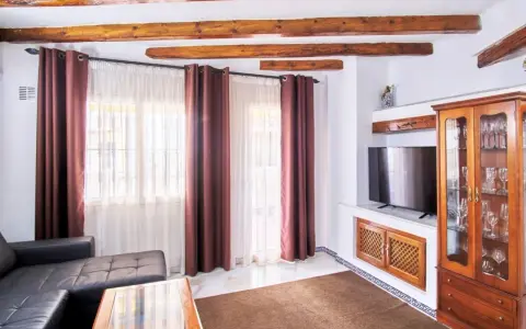 Salon z drewnianymi belkami na suficie, czarną kanapą i przeszkloną witryną. Zastanawiasz się, ile kosztuje wynajęcie mieszkania w Hiszpanii?