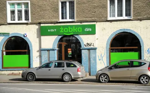 Przed sklepem Żabka, gdzie pewnie zastanawiamy się, ile żabka płaci za wynajem, stoją dwa samochody.