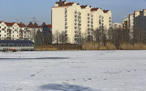 Zimowy krajobraz z zamarzniętym jeziorem i blokami mieszkalnymi w tle. Czy to zapowiedź, dlaczego ceny mieszkań w Warszawie mogą spaść nominalnie do końca 2026 roku?