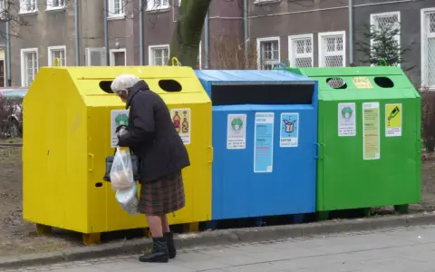 Starsza pani segreguje odpady przy kolorowych zsypach. Kto stoi za nowymi przepisami o segregacji odpadów w zsypach w starych blokach?