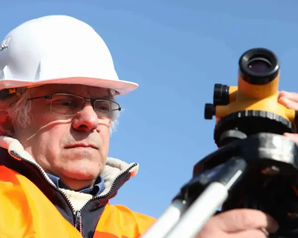 Geodeta w kasku i kamizelce odblaskowej pracuje z niwelatorem. Zastanawiasz się, ile kosztuje geodeta przy budowie domu?