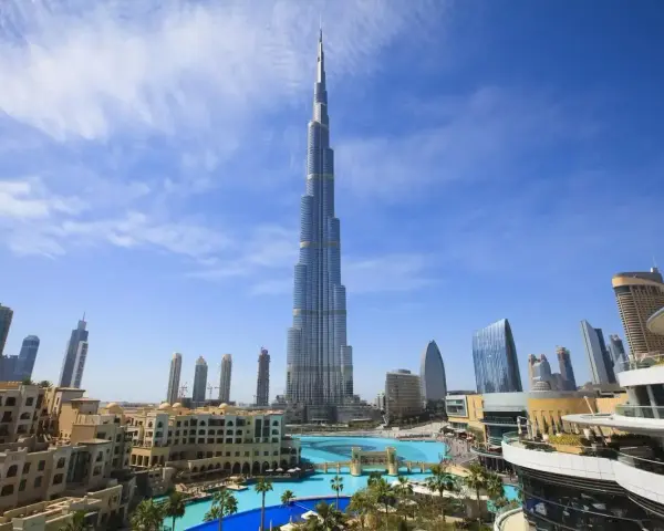 Burj Khalifa, najwyższy budynek świata, na tle błękitnego nieba z chmurami, otoczony nowoczesnymi budynkami i basenem.