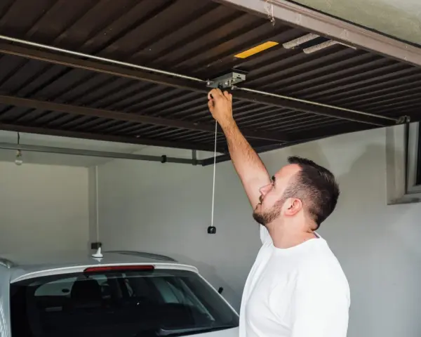 Mężczyzna sprawdza mechanizm bramy garażowej. Czy warto inwestować w garaże i miejsca postojowe przy obecnych cenach najmu?