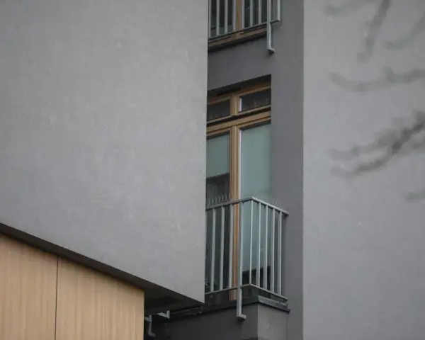 Szare ściany, drewniane elementy i wąskie okno z balkonem. To właśnie takie budynki budzą pytania, dlaczego mieszkańcy nowych osiedli masowo skarżą się na patodeweloperkę akustyczną.