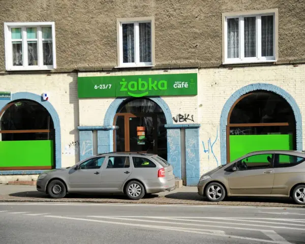 Przed sklepem Żabka, gdzie pewnie zastanawiamy się, ile żabka płaci za wynajem, stoją dwa samochody.