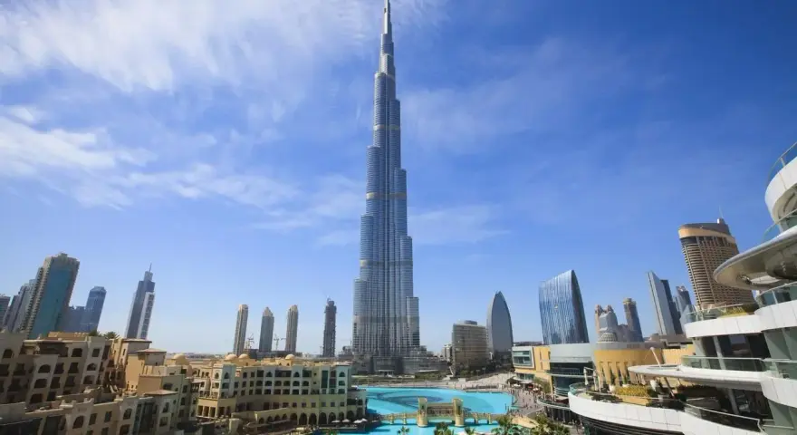 Burj Khalifa, najwyższy budynek świata, na tle błękitnego nieba z chmurami, otoczony nowoczesnymi budynkami i basenem.