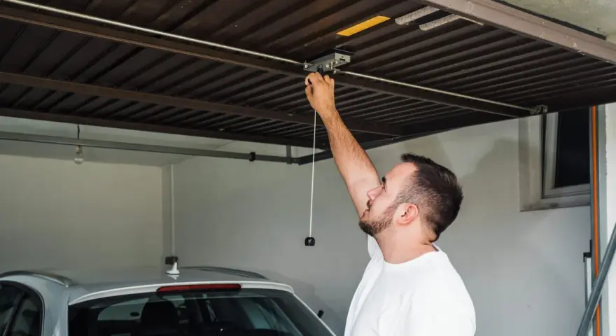 Mężczyzna sprawdza mechanizm bramy garażowej. Czy warto inwestować w garaże i miejsca postojowe przy obecnych cenach najmu?