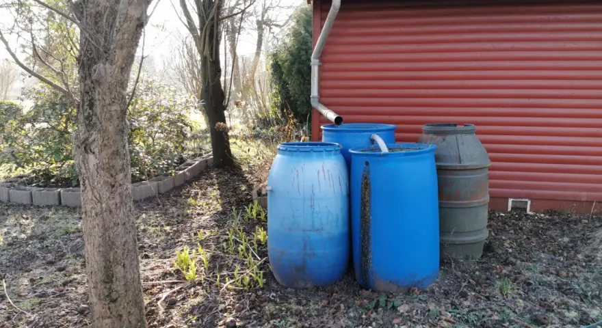 Zbiorniki na deszczówkę przy czerwonym budynku. Prawda o rzekomym opodatkowaniu deszczówki zbieranej na prywatnych posesjach jest taka, że nie ma takiego podatku.