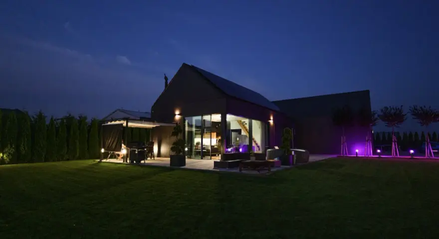 Nowoczesny dom nocą, z oświetlonym ogrodem i tarasem. Analiza prawdziwych kosztów eksploatacji domów pasywnych w polskich warunkach klimatycznych.