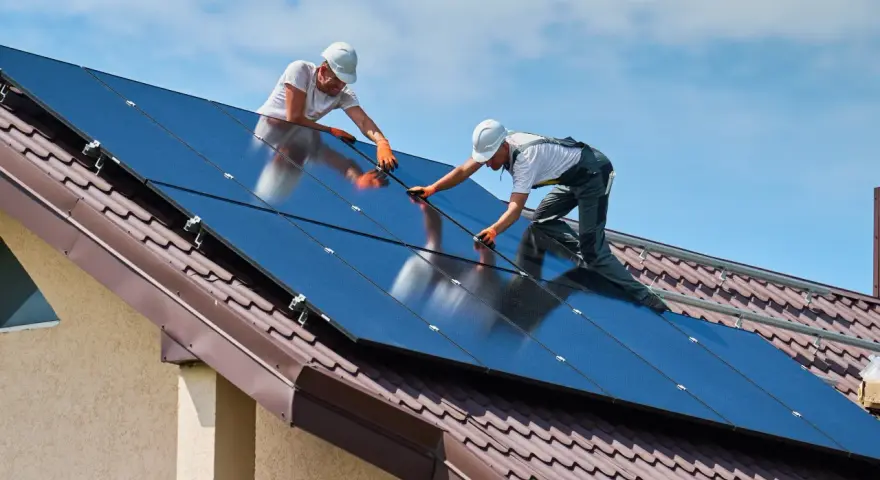 Dwóch monterów instaluje panele słoneczne na dachu. To przyszłość budownictwa, bo od września 2026 r. każdy nowy budynek musi posiadać magazyn energii.