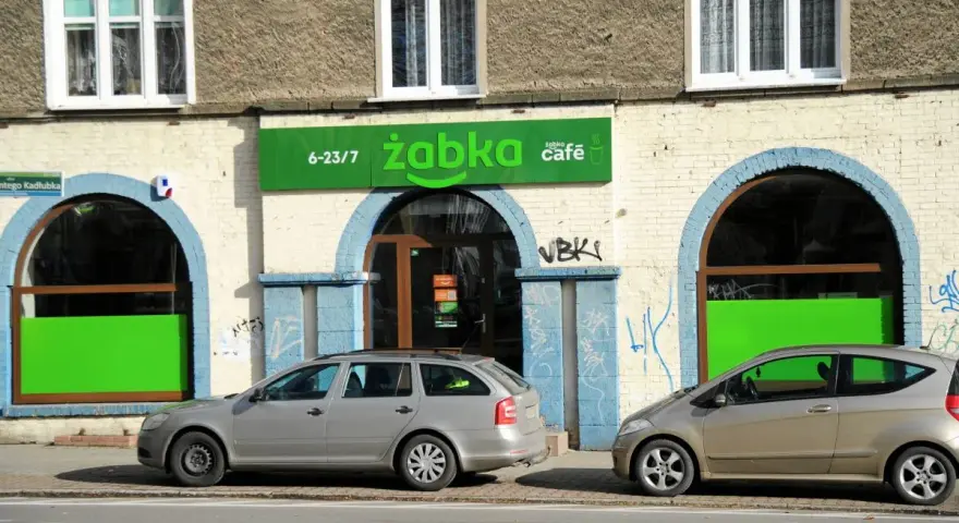 Przed sklepem Żabka, gdzie pewnie zastanawiamy się, ile żabka płaci za wynajem, stoją dwa samochody.