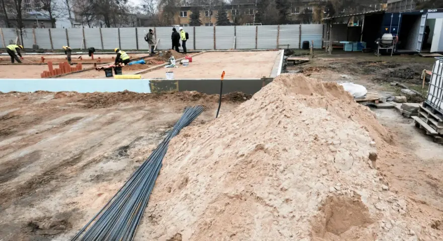 Budowa w marcu 2026. Działka z uregulowanym stanem prawnym, przygotowana pod fundamenty. Piasek, zbrojenie i pracownicy na placu budowy.