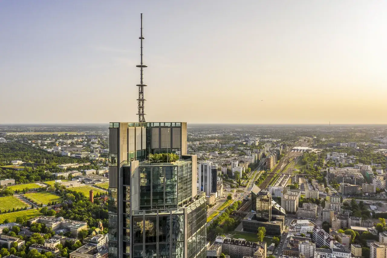 Widok z lotu ptaka na Varso Tower, najwyższy budynek w Polsce, z anteną na szczycie. W tle rozciąga się panorama Warszawy.