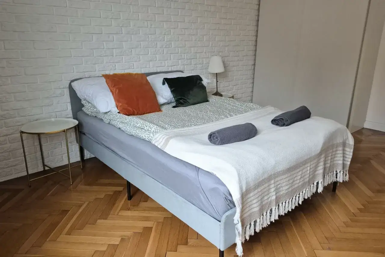 Przytulna sypialnia z łóżkiem, białym ceglanym murem i parkietem. Od 20 maja 2026 r. każdy lokal na Airbnb musi mieć numer rejestracyjny.