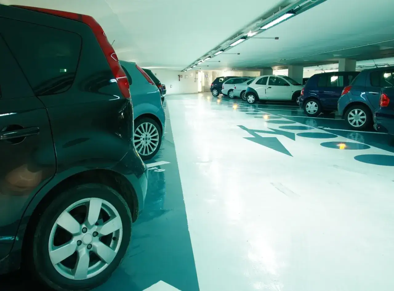 Czy parkingi podziemne w blokach są bezpieczne dla samochodów elektrycznych w 2026? Rzędy aut w podziemnym garażu, jasne oświetlenie, strzałki kierunkowe na podłodze.