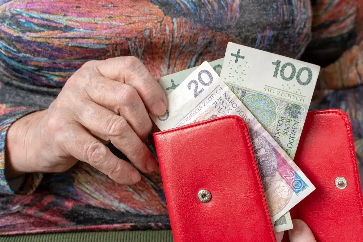 Dłoń starszej osoby wkłada banknoty do czerwonego portfela. Czy to odpowiedź na pytanie, dlaczego w marcu 2026 r. limity dochodowe do dodatku mieszkaniowego wzrosły o 20 proc.?
