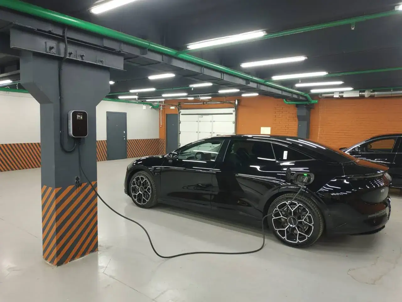 Czarny samochód elektryczny ładuje się w garażu. To przyszłość, dlaczego od września 2026 r. każdy blok musi mieć punkt ładowania aut elektrycznych.