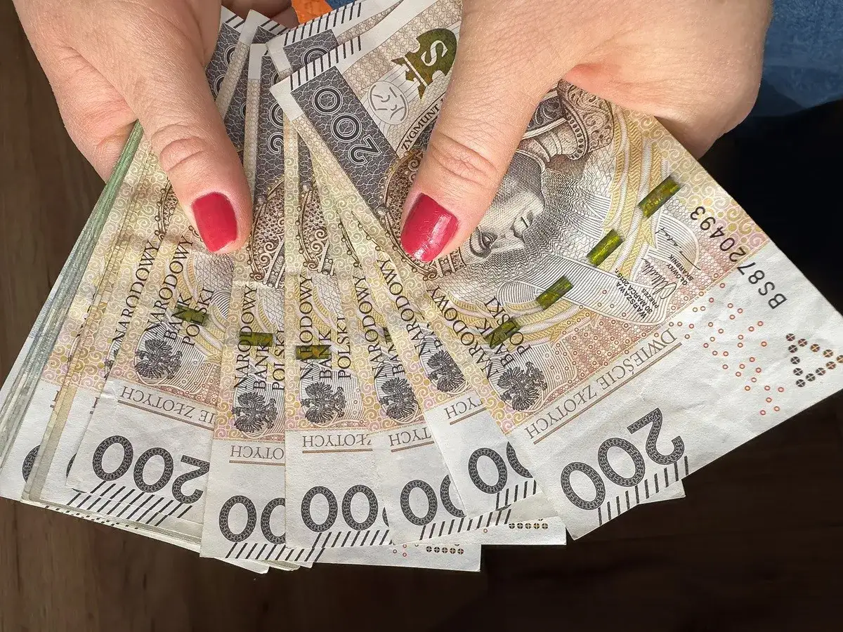 Dłonie trzymające stos banknotów 200 zł. Może to symbolizować wzrost dochodów, dlaczego w marcu 2026 r. limity dochodowe do dodatku mieszkaniowego wzrosły o 20 proc.