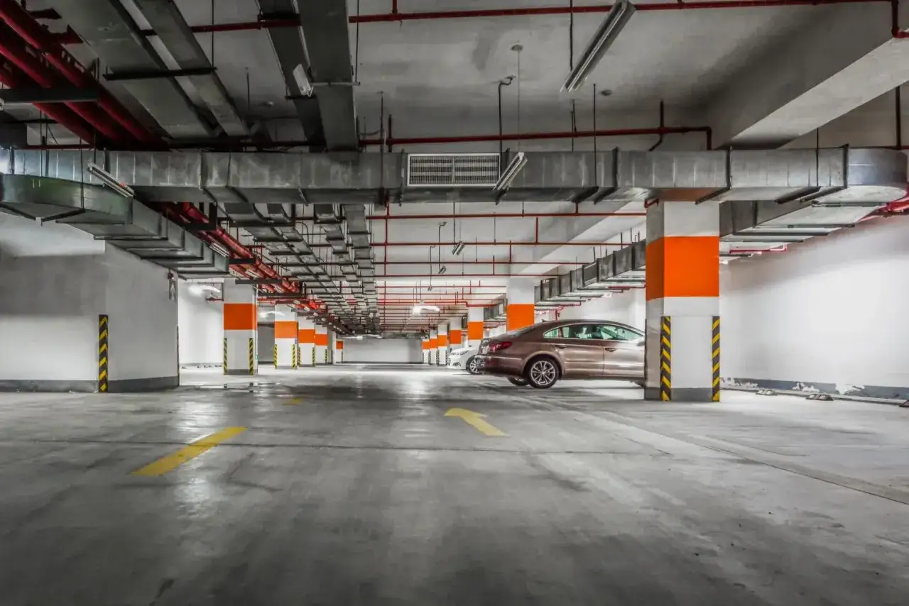 Podziemny parking z pomarańczowymi słupami i żółtymi strzałkami na posadzce. Czy warto inwestować w garaże i miejsca postojowe przy obecnych cenach najmu?