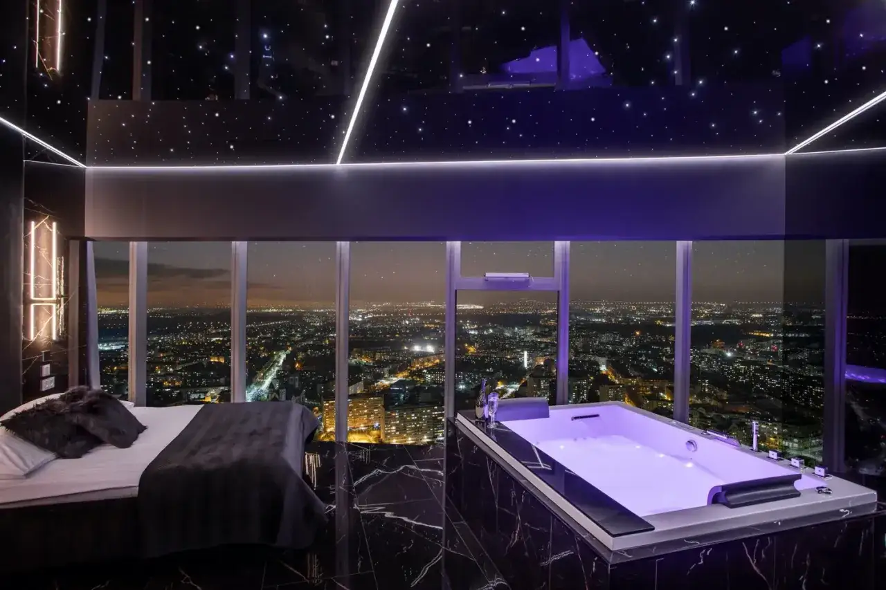 Luksusowy apartament z wanną i łóżkiem, z widokiem na nocne miasto. Nie wiadomo, ile pięter ma skytower, ale widok zapiera dech.