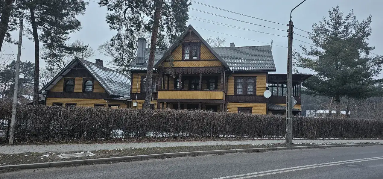 Sekrety licytacji komorniczych luksusowych domów celebrytów pod Warszawą. Drewniany dom z werandą i ozdobnymi detalami, otoczony zimową roślinnością.