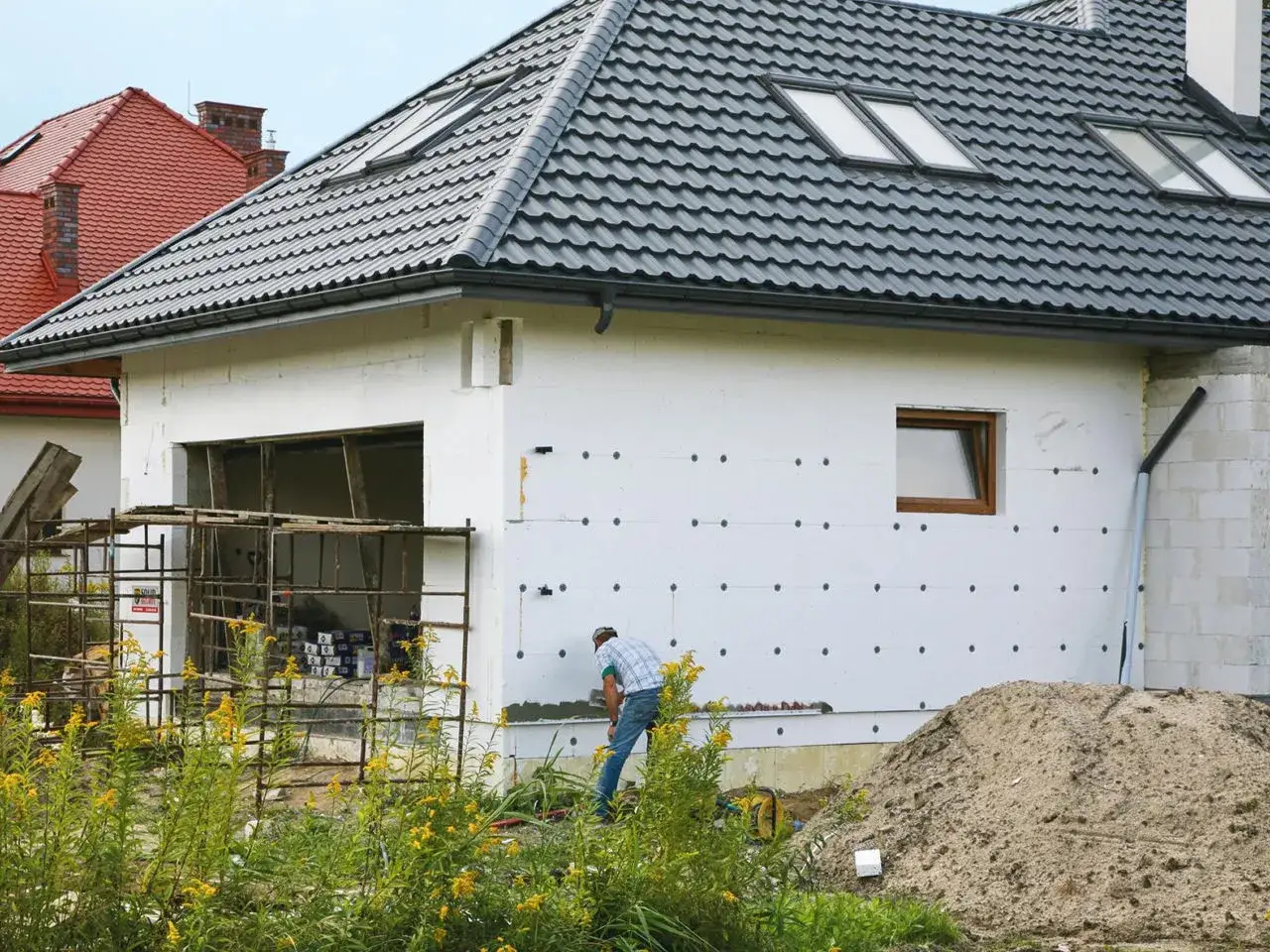 Budowa domu w trakcie, pracownik ociepla ścianę. Czy ocieplenie bloku wełną mineralną jest lepsze niż styropianem pod kątem pożarowym?