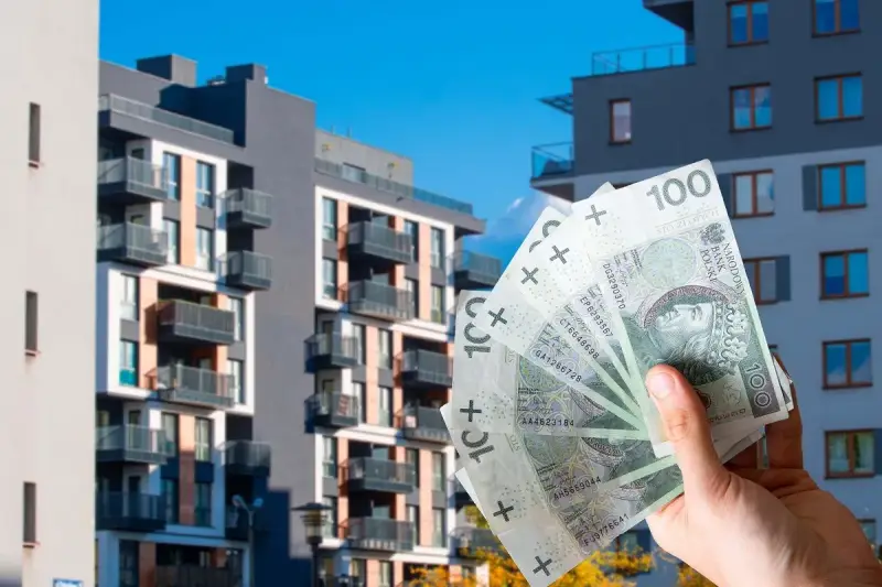 Kto stoi za kampanią "mieszkanie za 10 tysięcy"? Czy to realna cena za metr? Dłoń z banknotami 100 zł na tle nowoczesnych bloków.